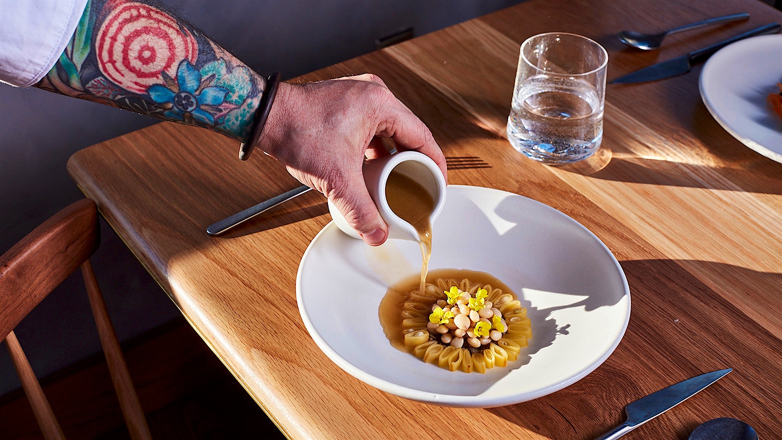 Chef Brock's arm pouring a sauce over a delicately patterned bowl of beans.